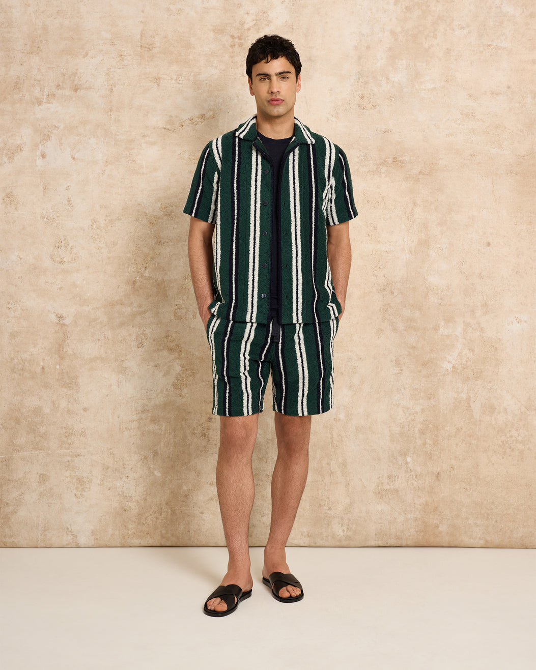Man wearing a green and white striped outfit against a beige wall.