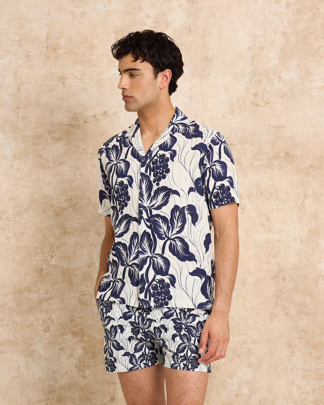Man wearing a navy floral shirt and shorts set against a beige background