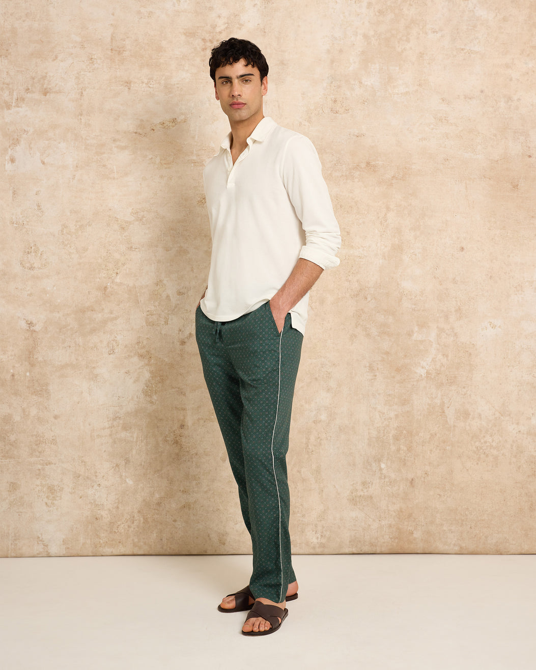 Man wearing a white shirt and green pants against a beige wall