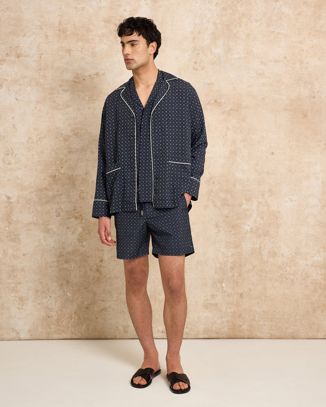 Man wearing a navy patterned set against a beige wall.
