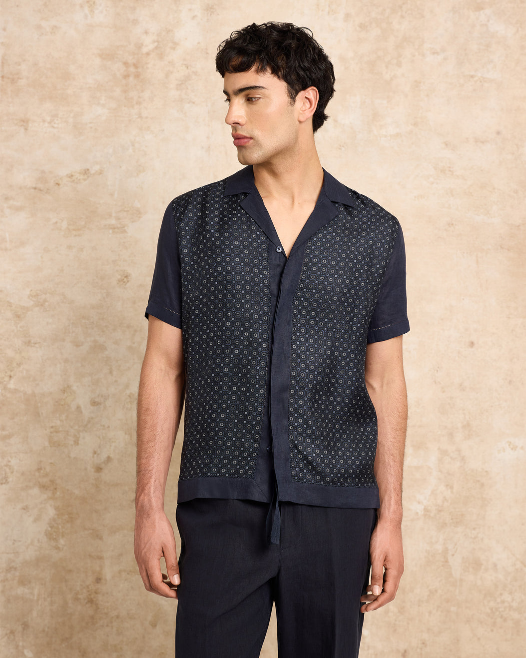 Man wearing a navy patterned shirt over a black base shirt on a beige background