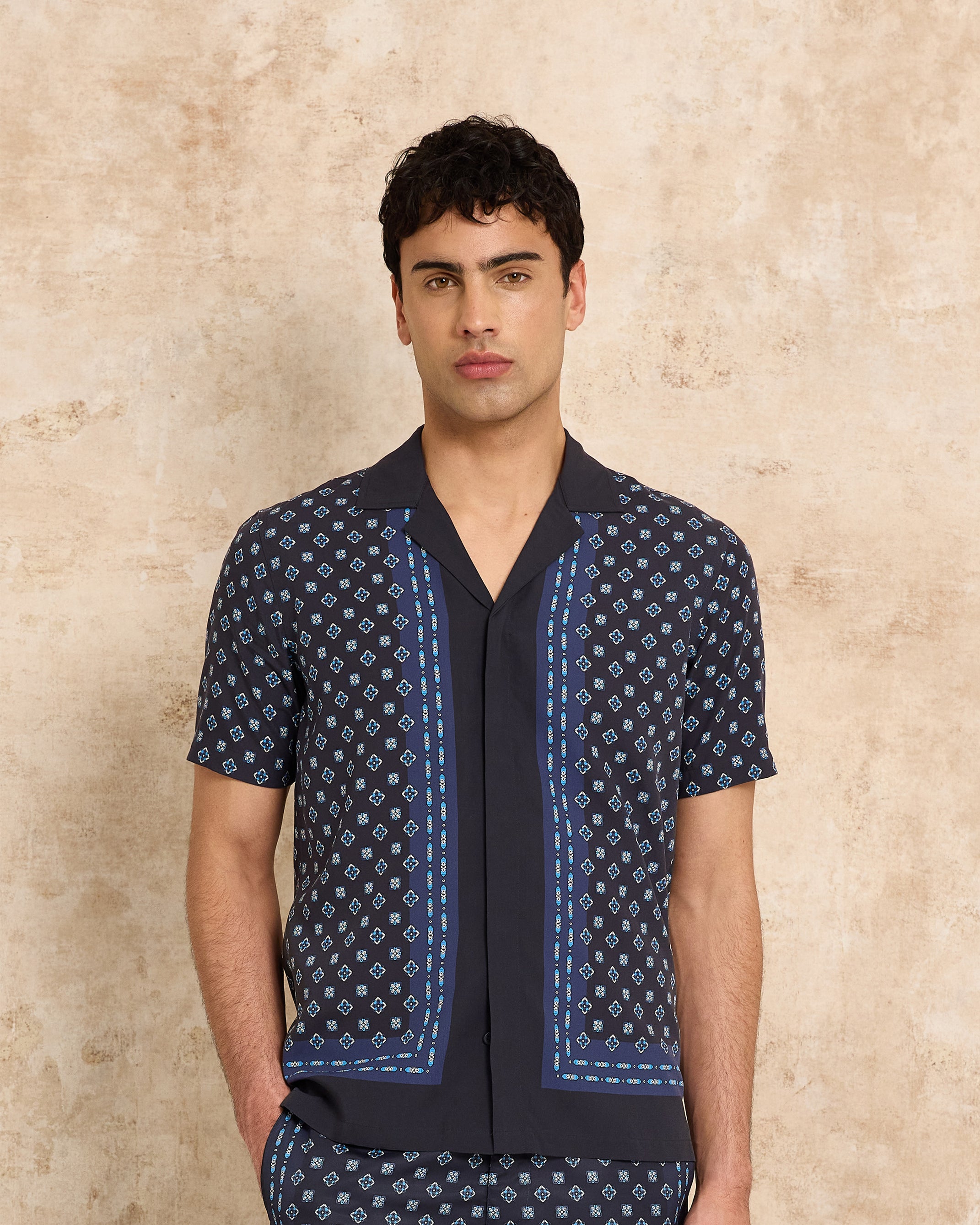 Man wearing a navy patterned shirt against a beige background