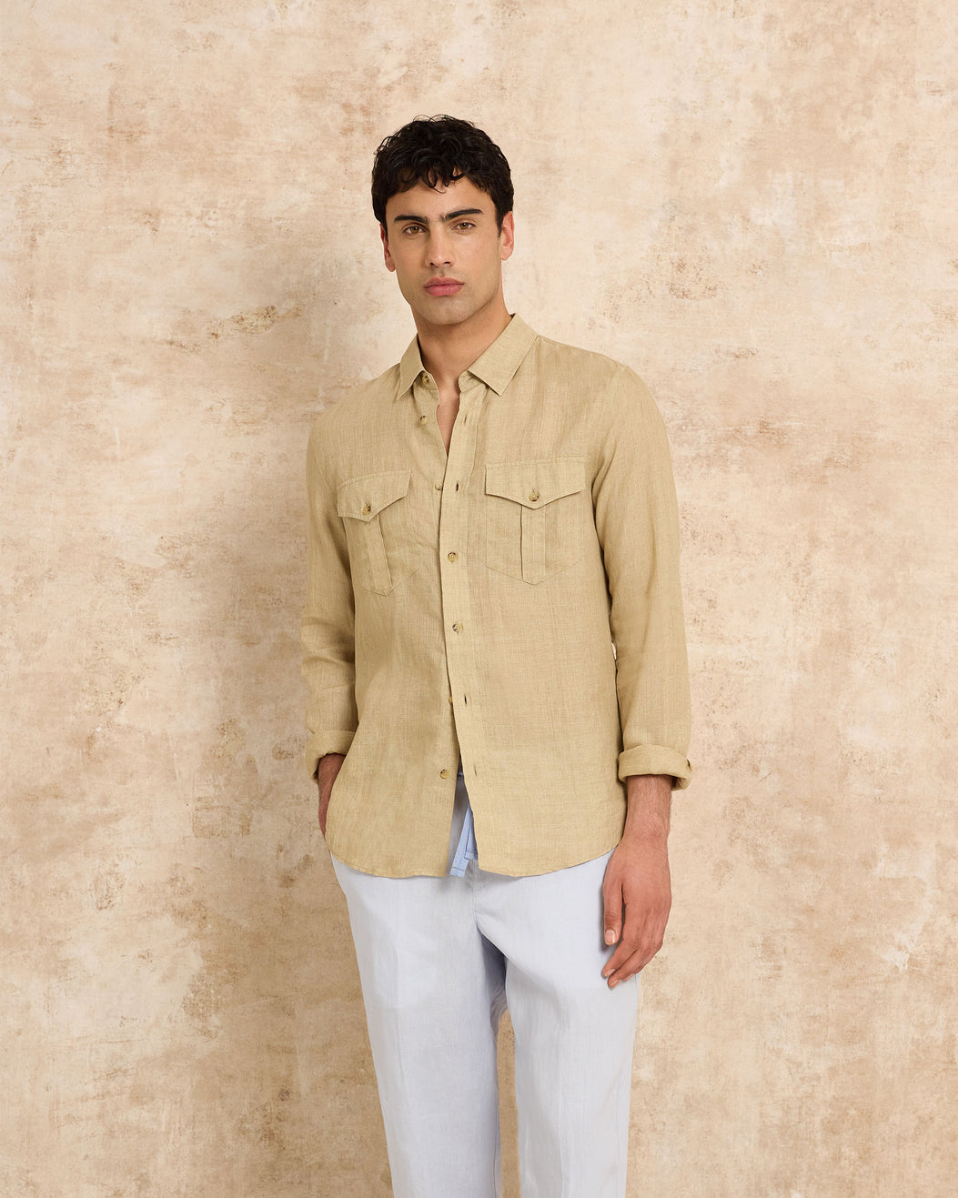 Man wearing a beige shirt and light blue pants against a beige wall