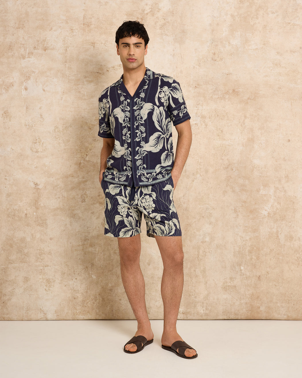 Man wearing a navy blue floral set against a beige wall